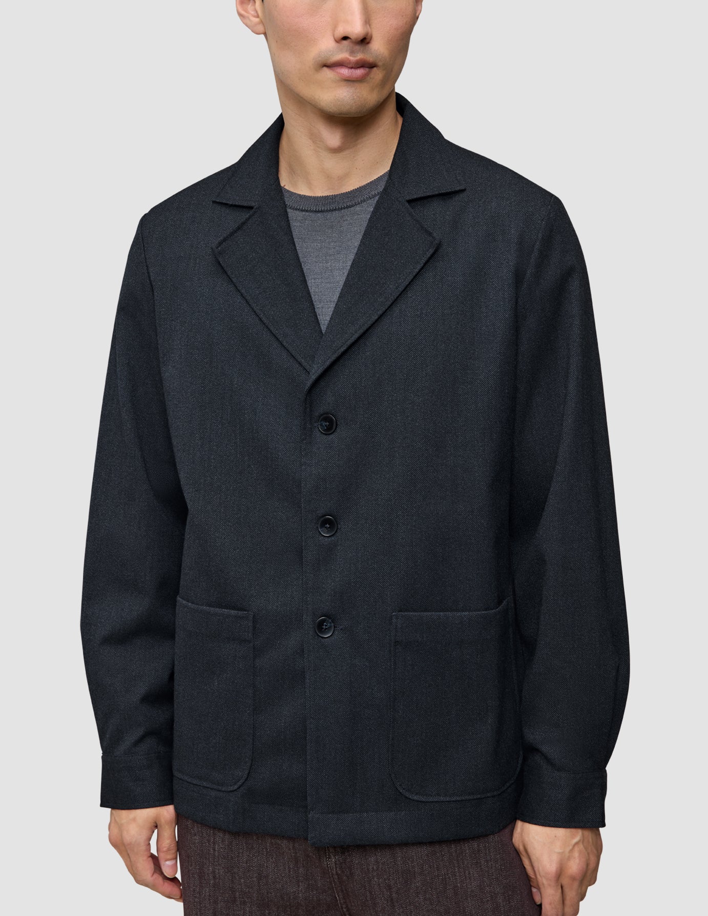 En mand bærer en Atelier Overshirt i mørk marineblå med en krave med udskæring, to påsatte lommer foran og en pasform i blazerstil.